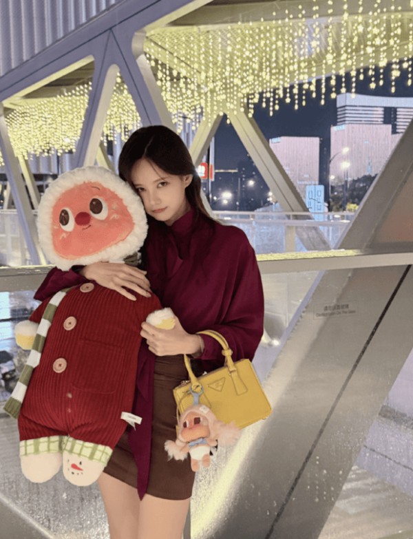 李一桐穿酒红色上衣，亲昵抱着圆萌玩偶。