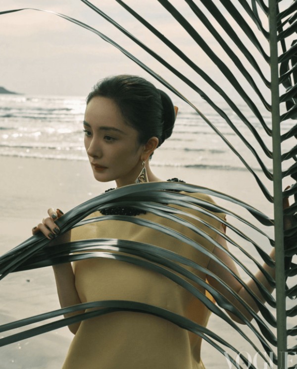 杨幂手持棕榈叶轻遮身侧，暖调造型衬得气色柔和。