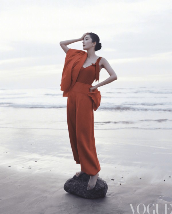 杨幂身着红装立于海边，抬手轻抵脖颈的姿态利落明艳。