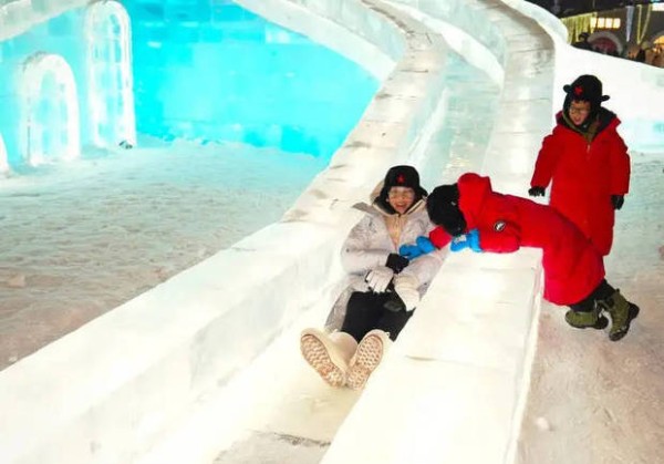 胡杏儿登上冰做成的滑梯，两个小孩在身旁陪着她。