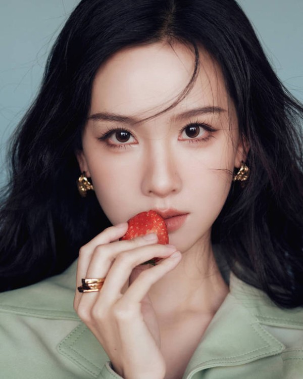 陈都灵手持草莓轻贴唇边，神态灵动。